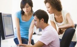 Three people sitting in computer room looking at monitor